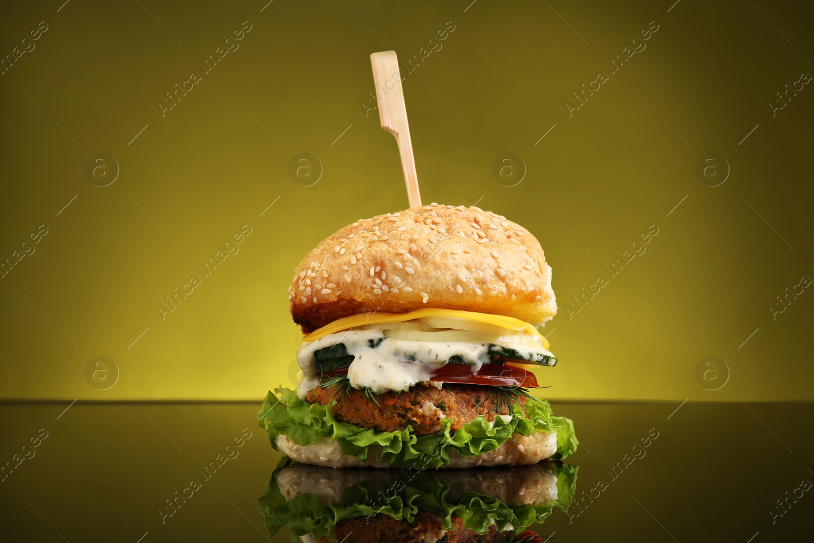 Photo of Delicious vegetarian burger on mirror surface against olive background