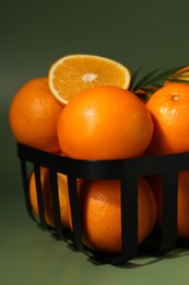 Photo of Fresh oranges in metal basket on green background, closeup