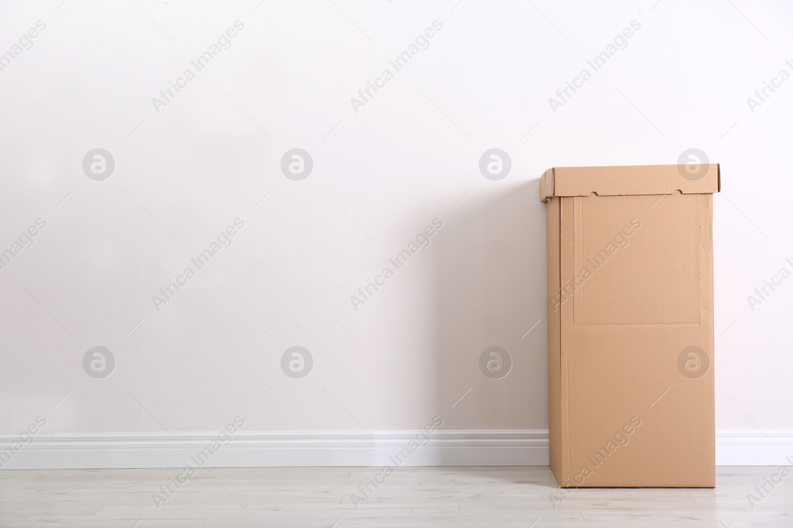 Photo of Cardboard wardrobe box against light wall indoors. Space for text