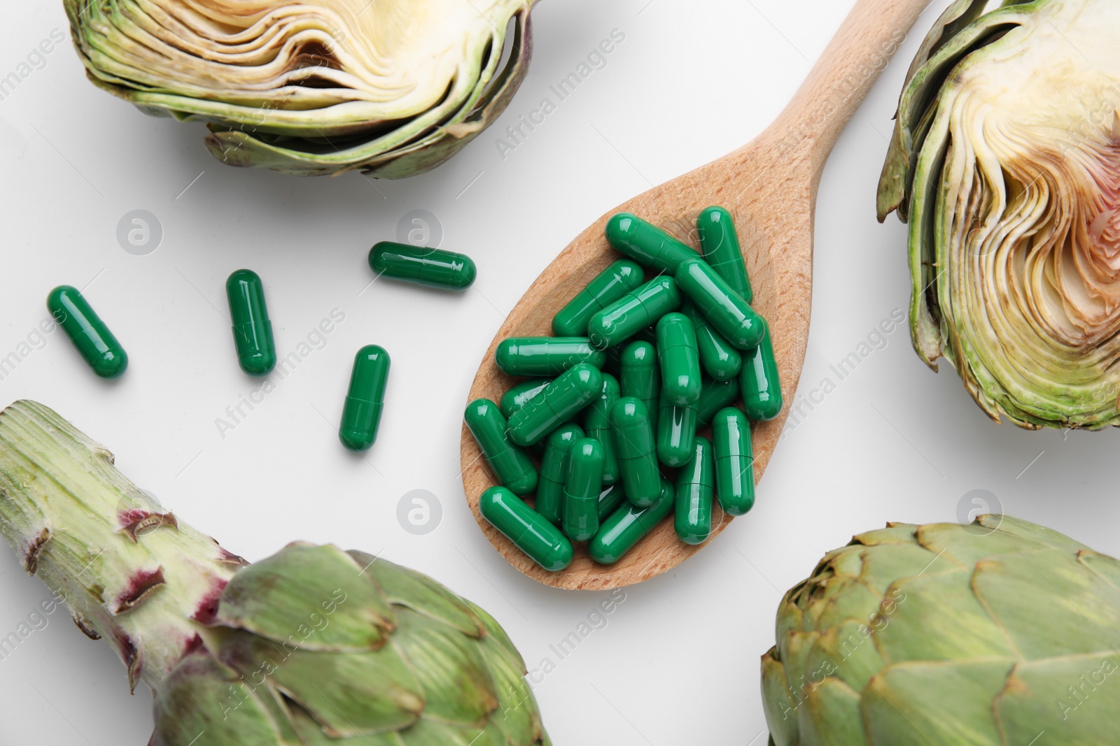 Photo of Spoon with pills and fresh artichokes on white background, flat lay