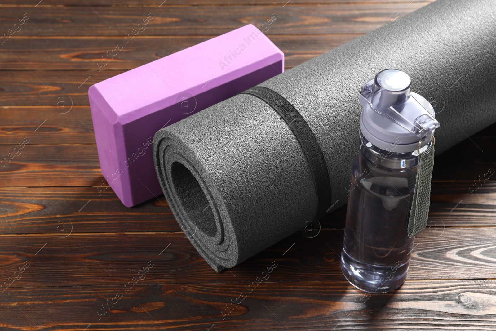 Photo of Exercise mat, yoga block and bottle of water on wooden floor