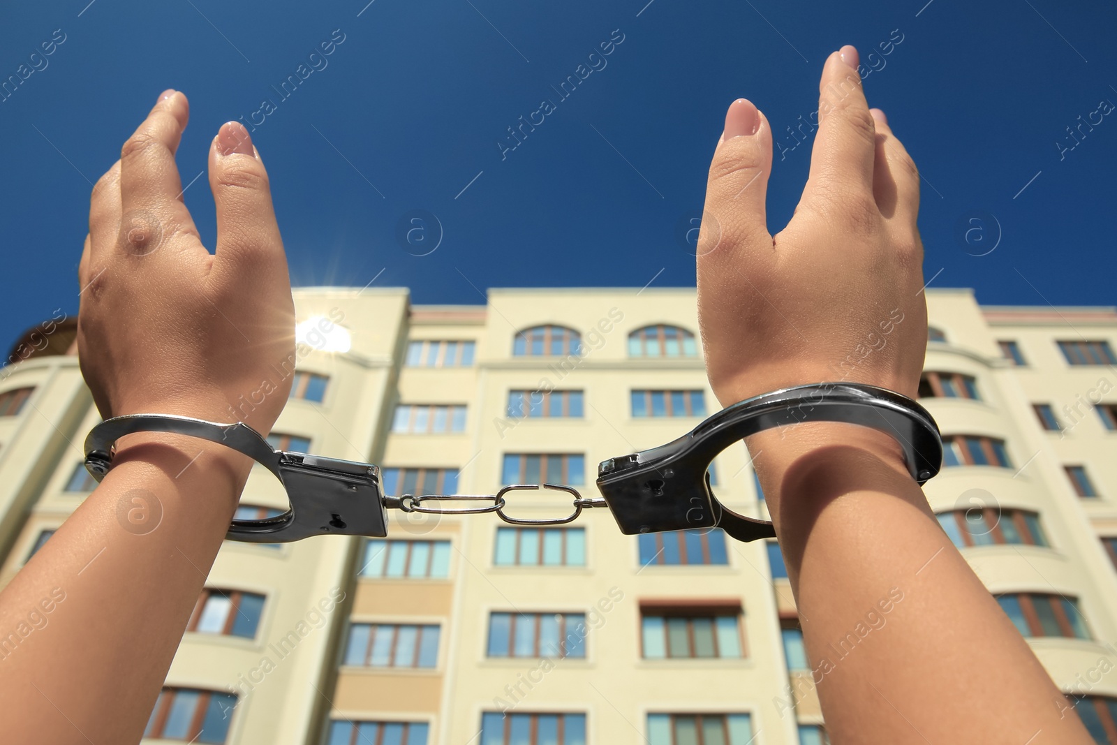 Photo of Woman in handcuffs against building under blue sky, closeup