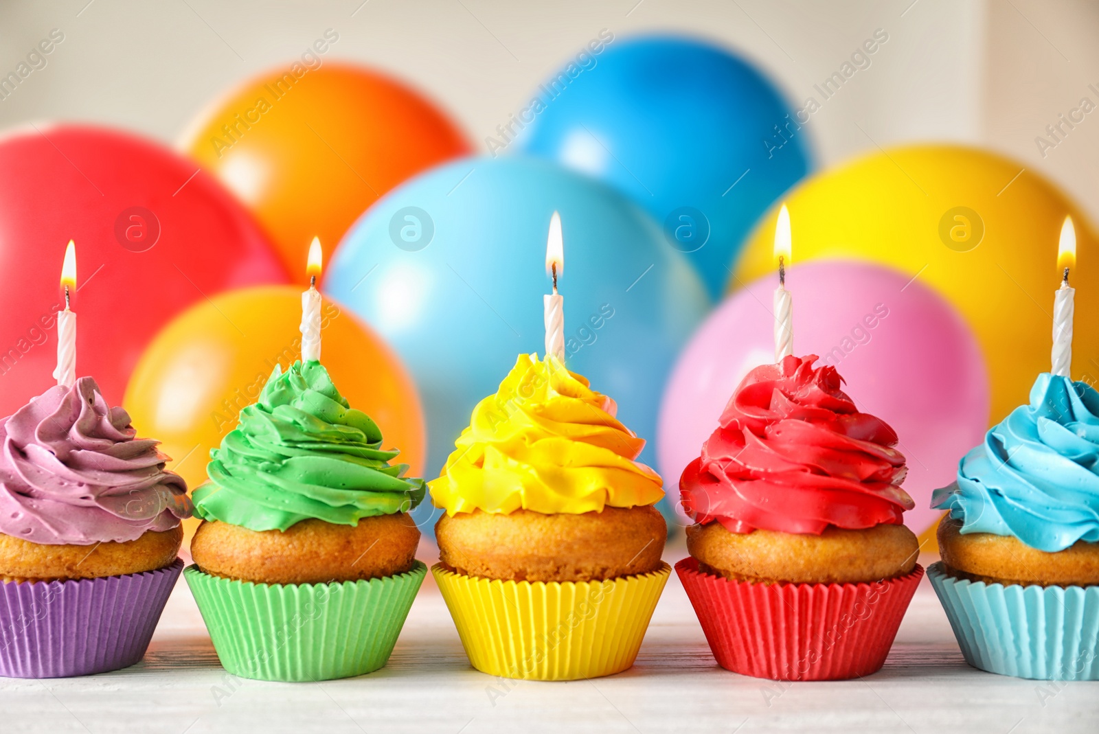 Photo of Delicious birthday cupcakes with candles and blurred balloons on background