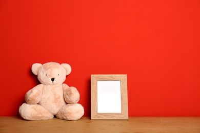 Photo of Teddy bear and photo frame on table against red background, space for text. Child room interior