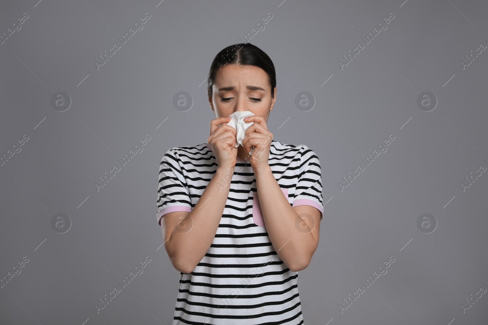 Photo of Sick young woman sneezing in tissue on grey background. Cold symptoms