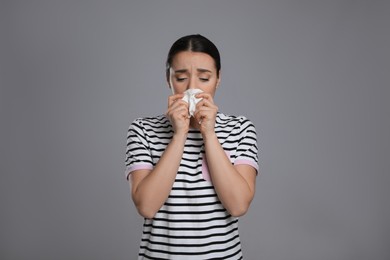 Photo of Sick young woman sneezing in tissue on grey background. Cold symptoms