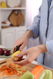 Woman peeling fresh potato at table indoors, closeup