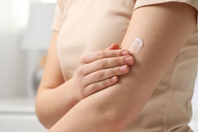 Young woman with dry skin applying cream onto her arm indoors, closeup