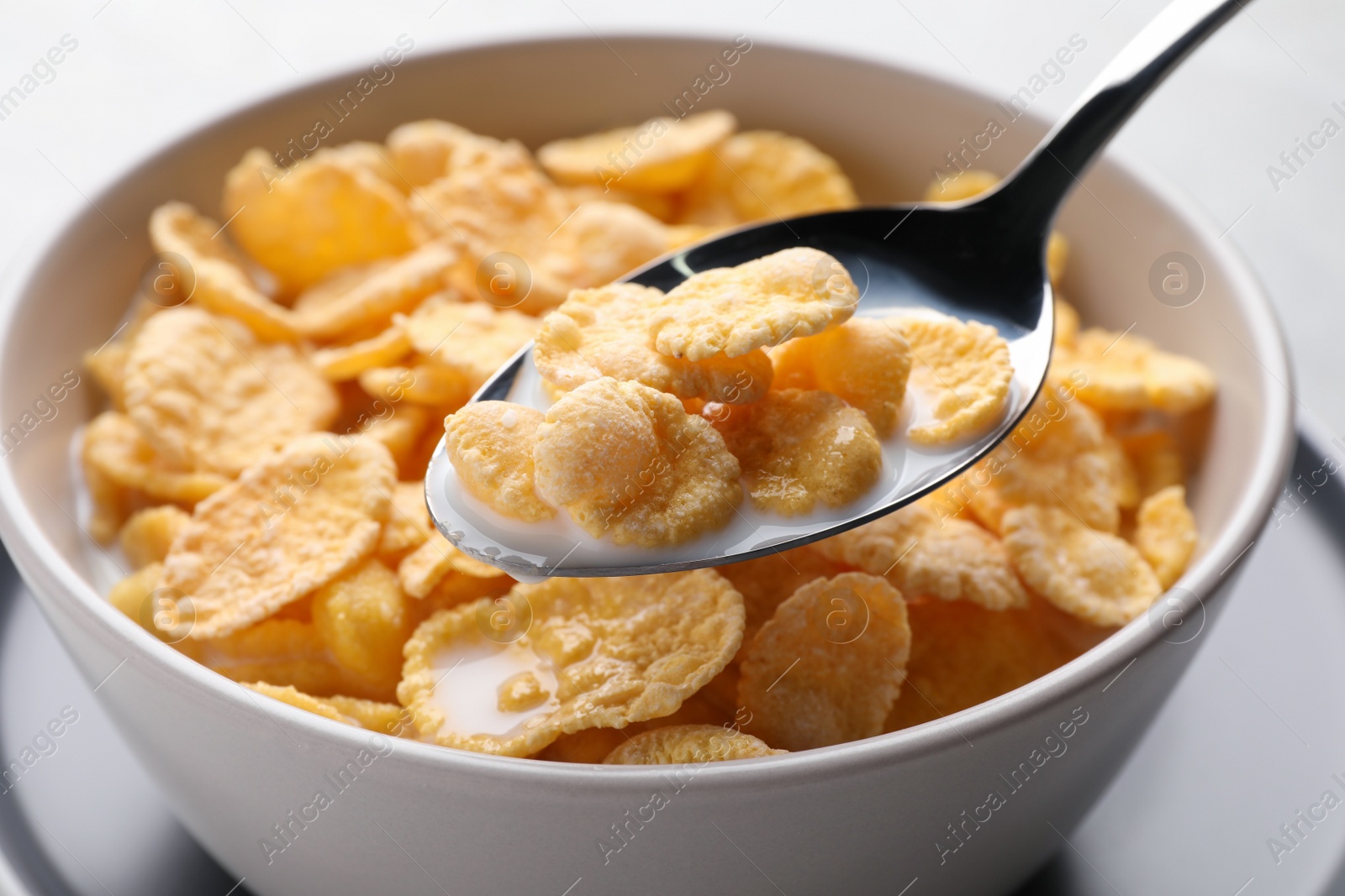 Photo of Spoon with tasty cornflakes and milk over bowl, closeup