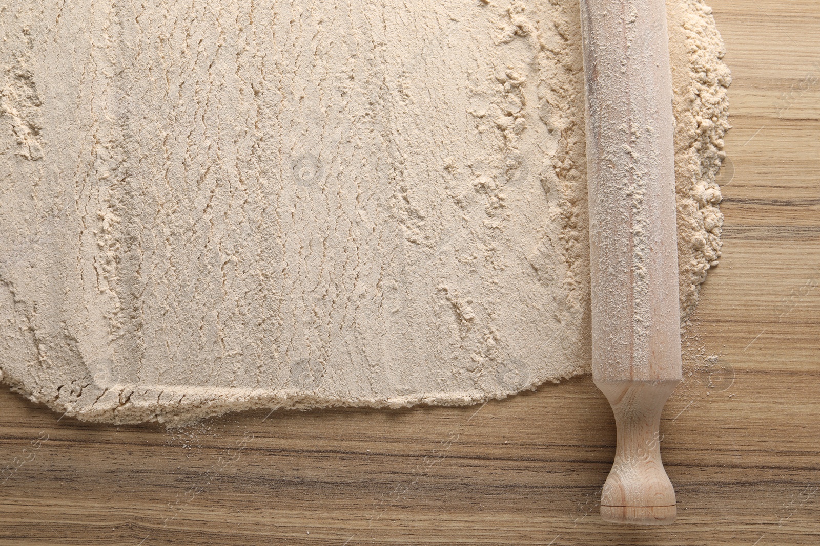 Photo of Flour and rolling pin on wooden table, top view