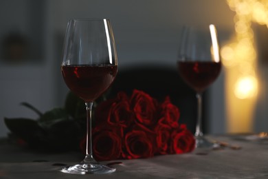 Photo of Glasses of red wine and rose flowers on grey table against blurred lights, space for text. Romantic atmosphere