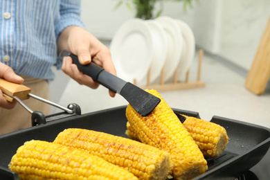 Photo of Woman taking corn from grill pan with tongs in kitchen, closeup