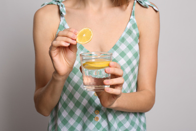 Photo of Young woman with glass of lemon water on light background, closeup