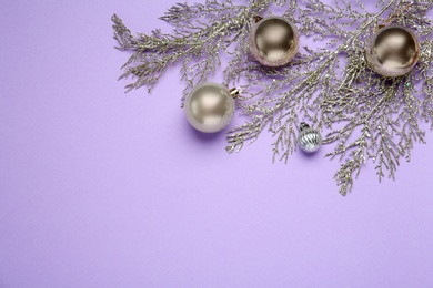 Photo of Shiny Christmas balls and decorative coniferous branches on violet background, flat lay with space for text