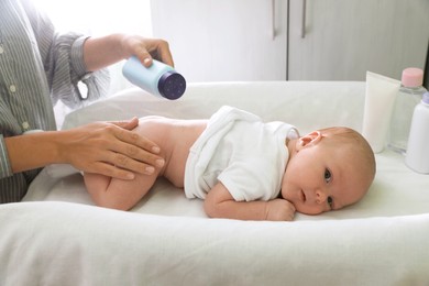 Photo of Mother applying dusting powder at baby's buttocks on changing table indoors, closeup