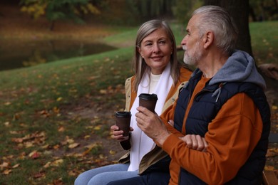 Photo of Affectionate senior couple with cups of coffee in autumn park, space for text