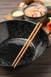 Black wok, chopsticks and products on color wooden table, closeup