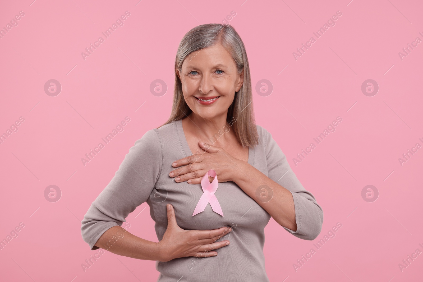 Photo of Beautiful senior woman with pink ribbon on color background. Breast cancer awareness