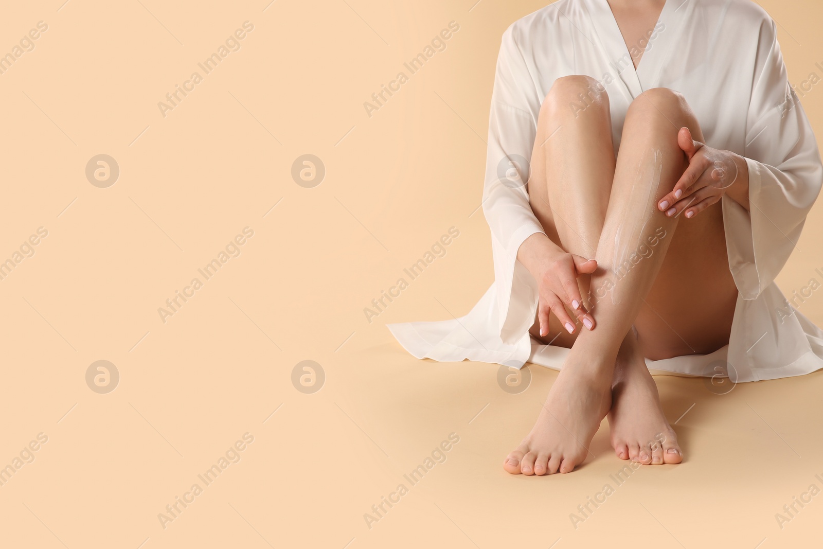 Photo of Woman applying body cream onto her smooth legs on beige background, closeup. Space for text