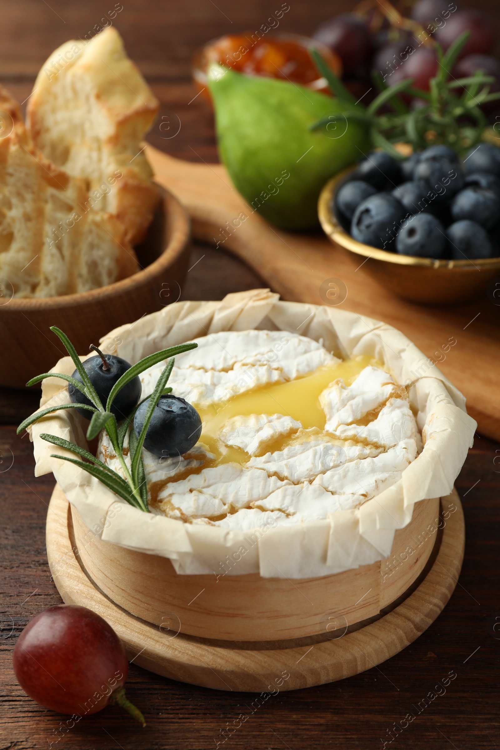 Photo of Tasty baked brie cheese and products on wooden table