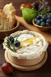 Tasty baked brie cheese and products on wooden table