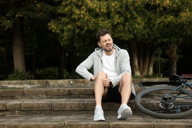 Man with injured knee on steps near bicycle outdoors, space for text