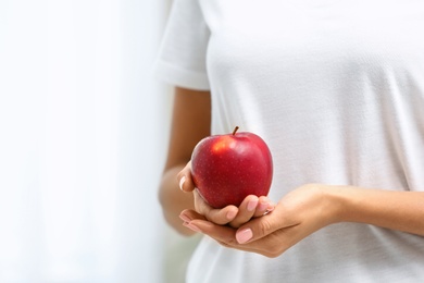 Photo of Woman holding fresh red apple on light background, closeup. Space for text