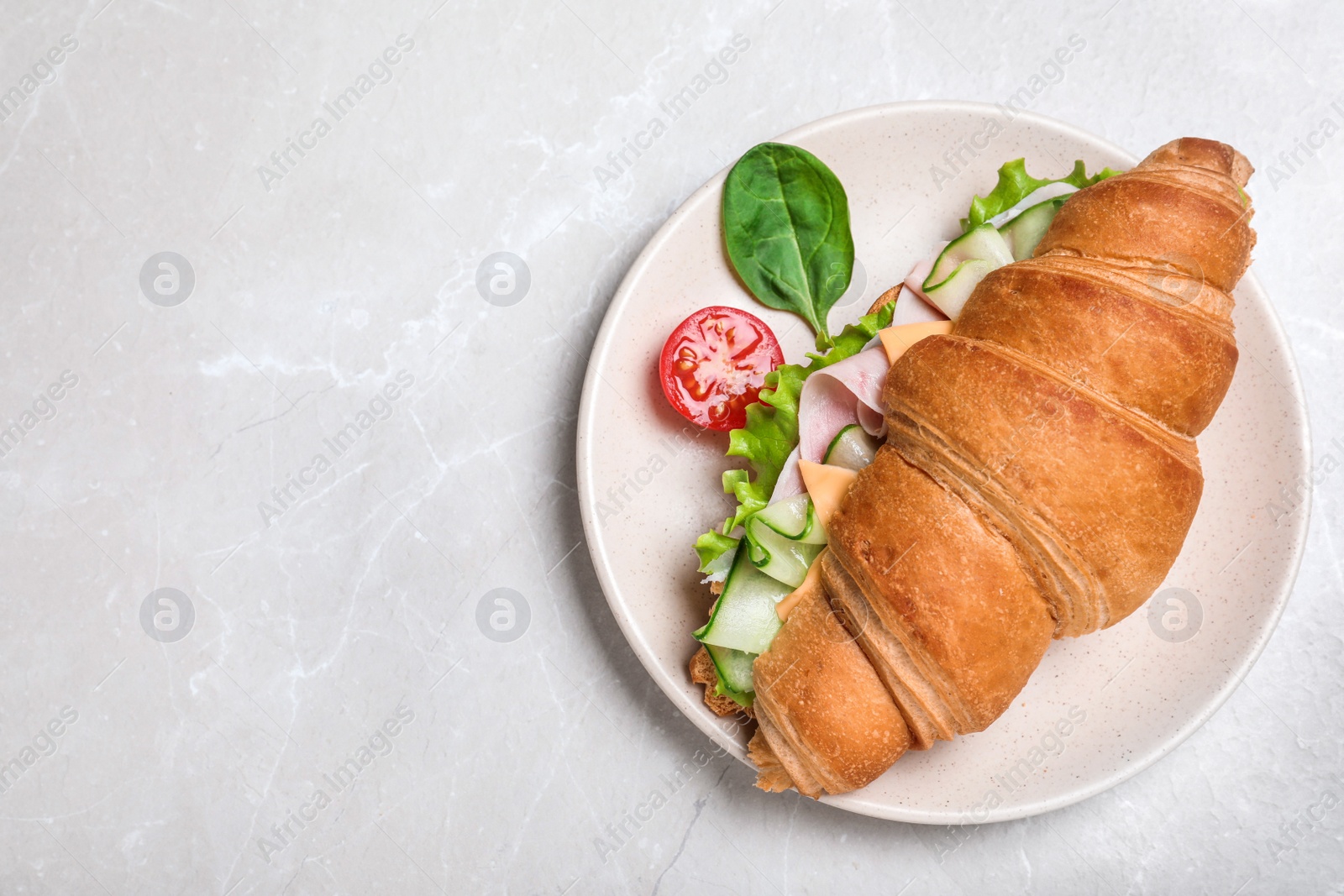 Photo of Tasty croissant sandwich with ham and cucumber on light grey marble table, top view. Space for text