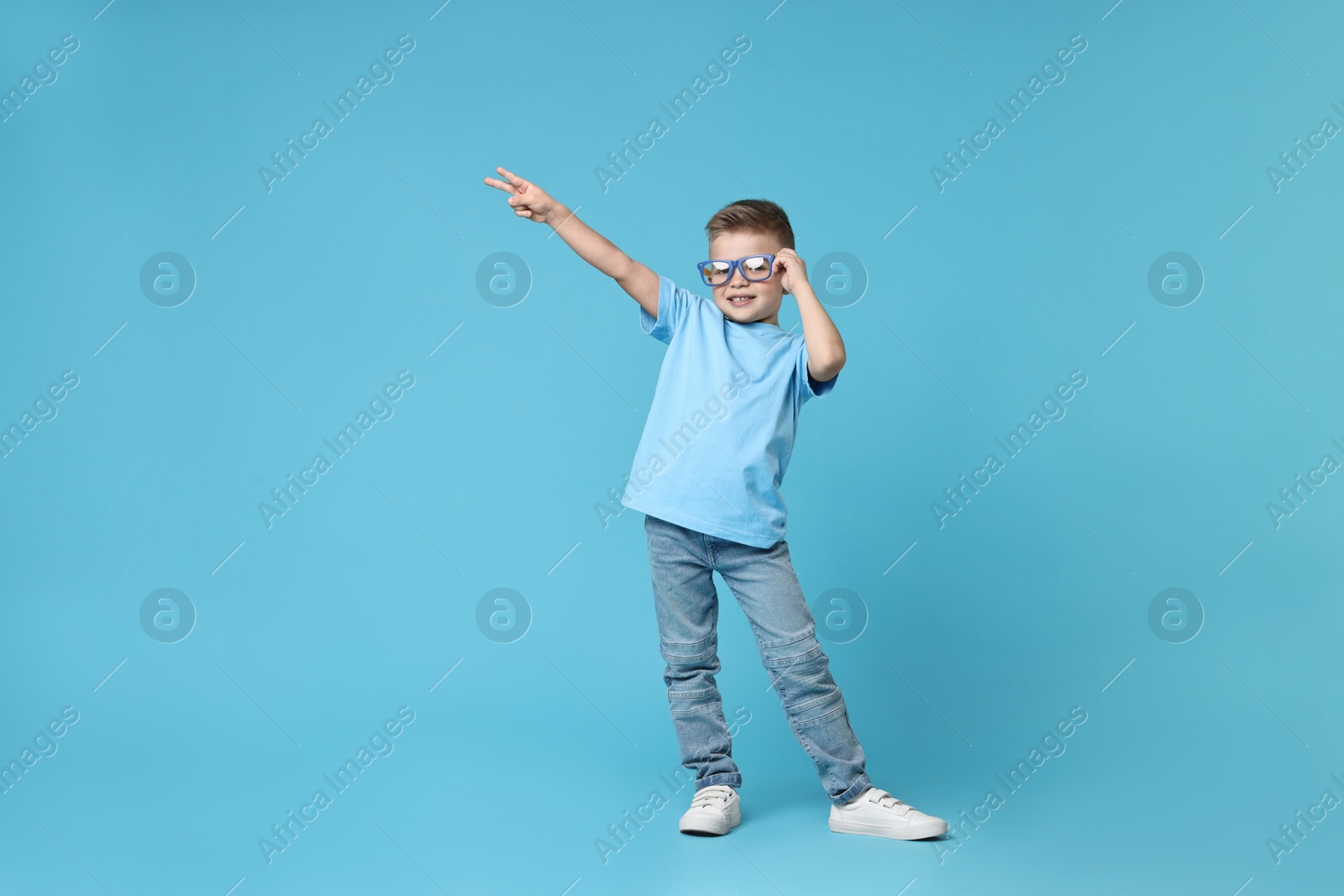 Photo of Happy little boy dancing on light blue background. Space for text