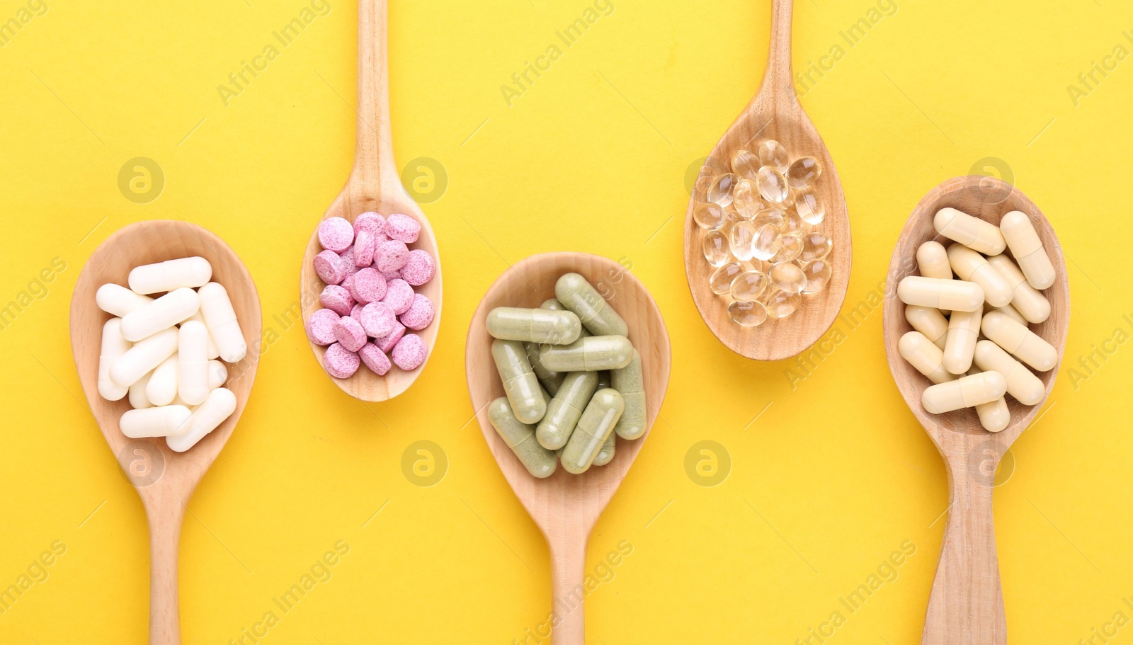 Photo of Different vitamin pills in wooden spoons on yellow background, flat lay