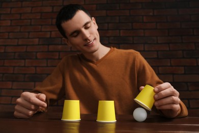 Photo of Shell game. Man showing ball under cup at wooden table, low angle view