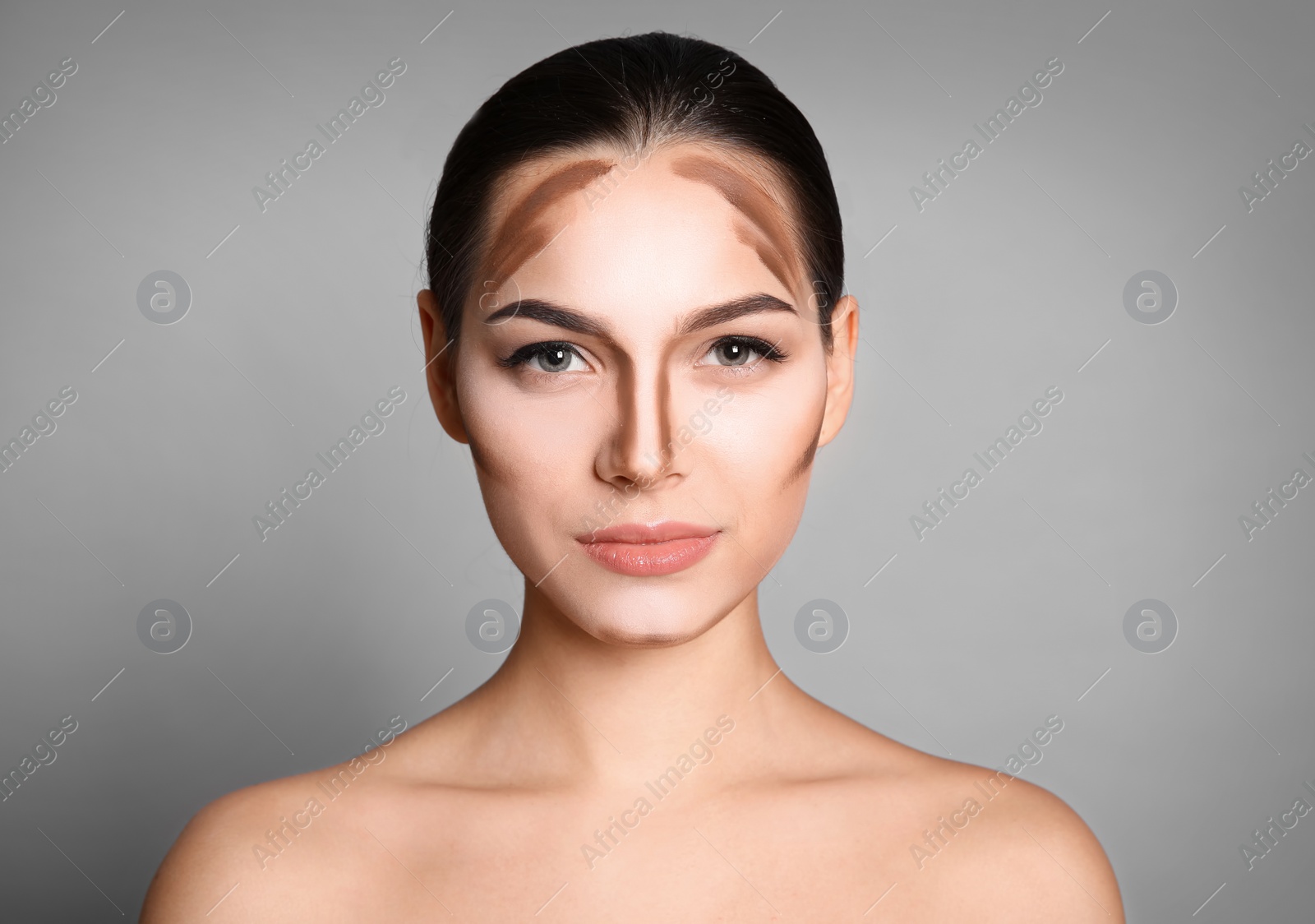 Photo of Young woman with contouring lines on her face against grey background. Professional makeup products