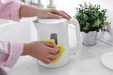 Photo of Woman cleaning electric kettle with sponge at countertop in kitchen, closeup
