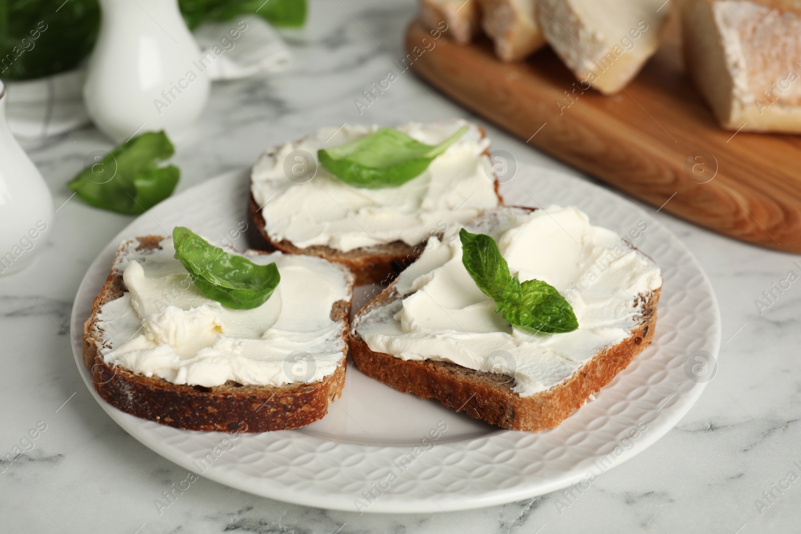 Photo of Bread with cream cheese and basil on white marble table