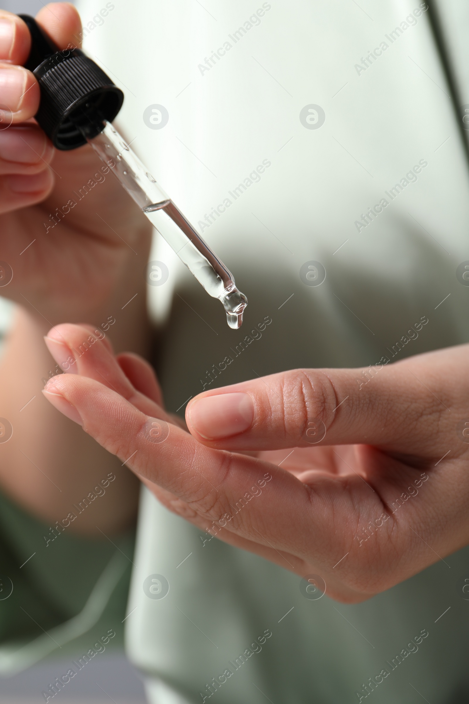 Photo of Woman applying cosmetic serum onto hand on blurred background, closeup