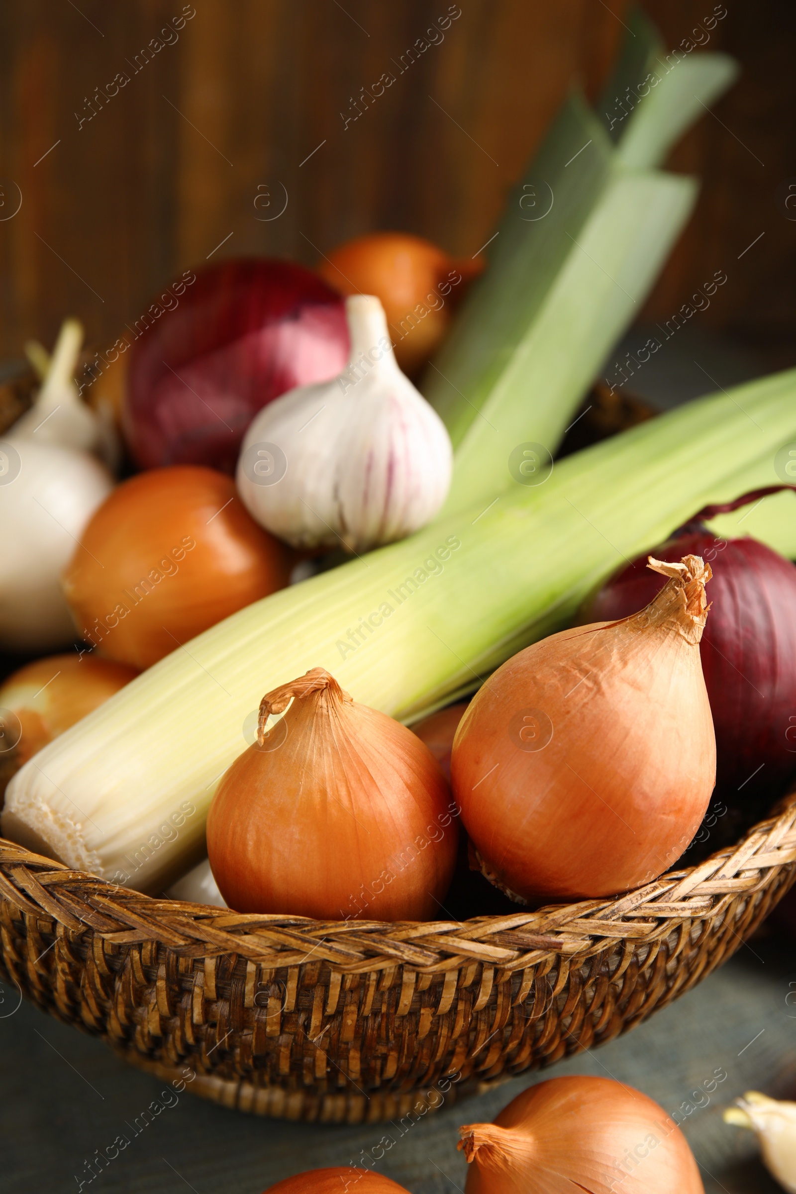 Photo of Wicker basket with fresh onion bulbs, leeks and garlic on light blue wooden table, closeup