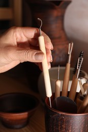 Woman taking clay crafting tool from cup in workshop, closeup