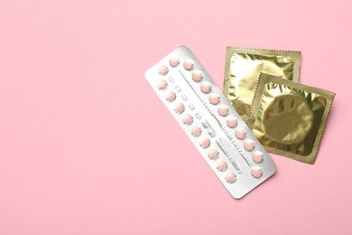 Photo of Condoms and birth control pills on pink background, top view with space for text. Safe sex