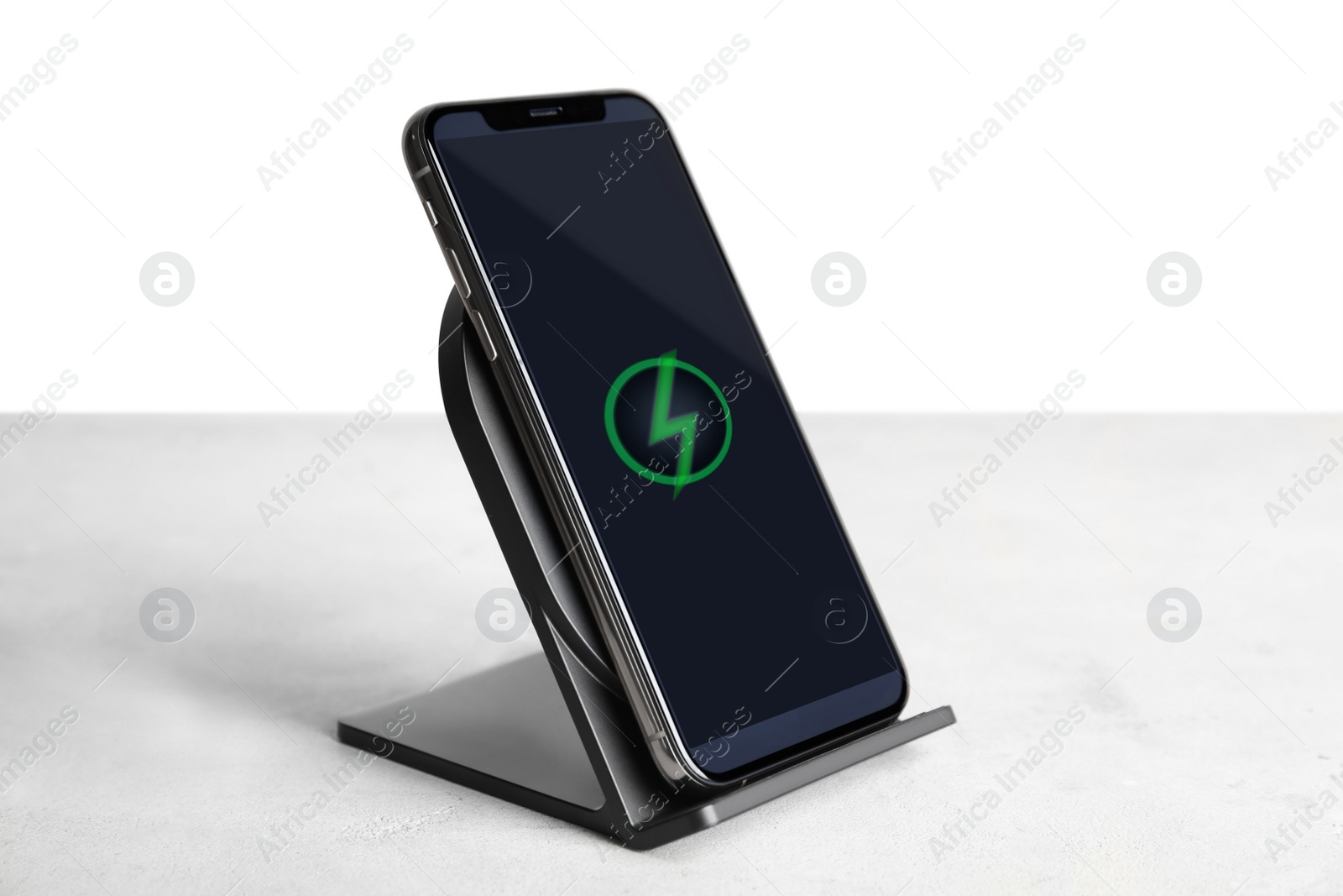 Photo of Mobile phone charging with wireless pad on light stone table