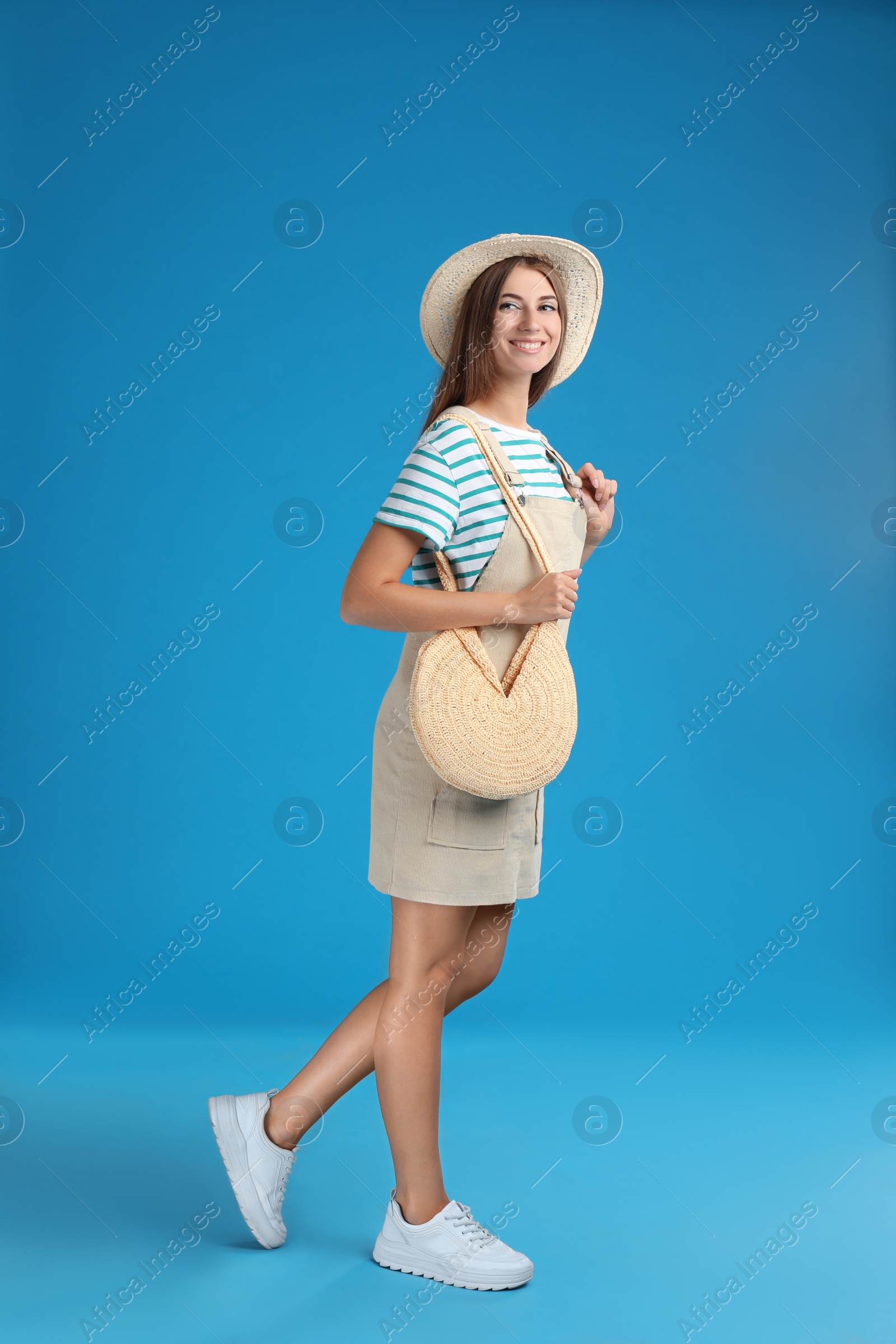 Photo of Beautiful young woman with stylish straw bag on light blue background