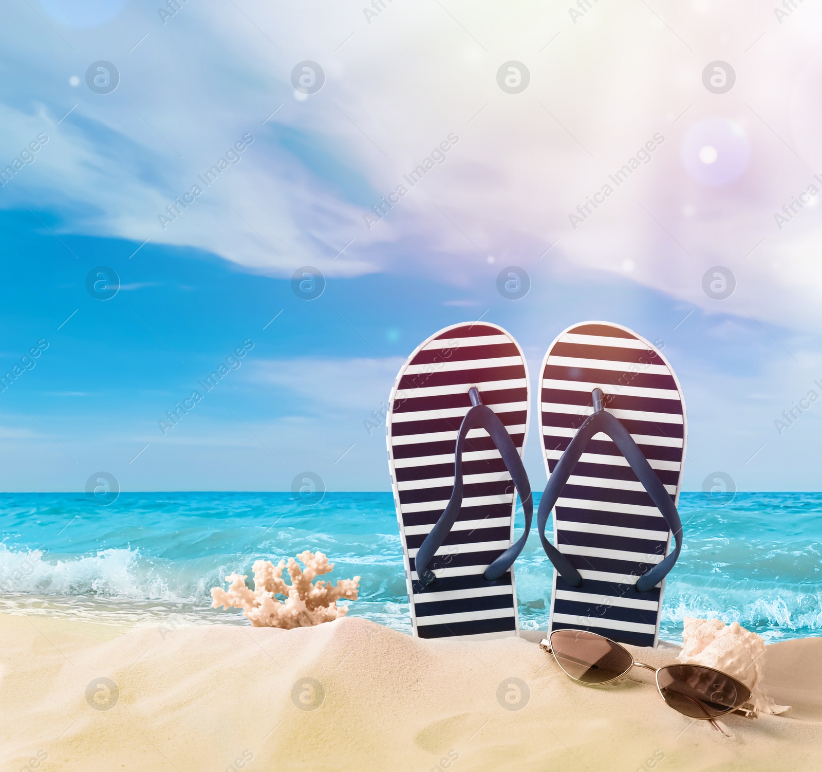 Image of Striped flip flops, coral, sea shell and sunglasses on sandy beach 