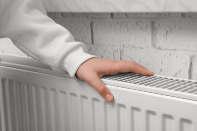 Photo of Girl warming hand on heating radiator indoors, closeup