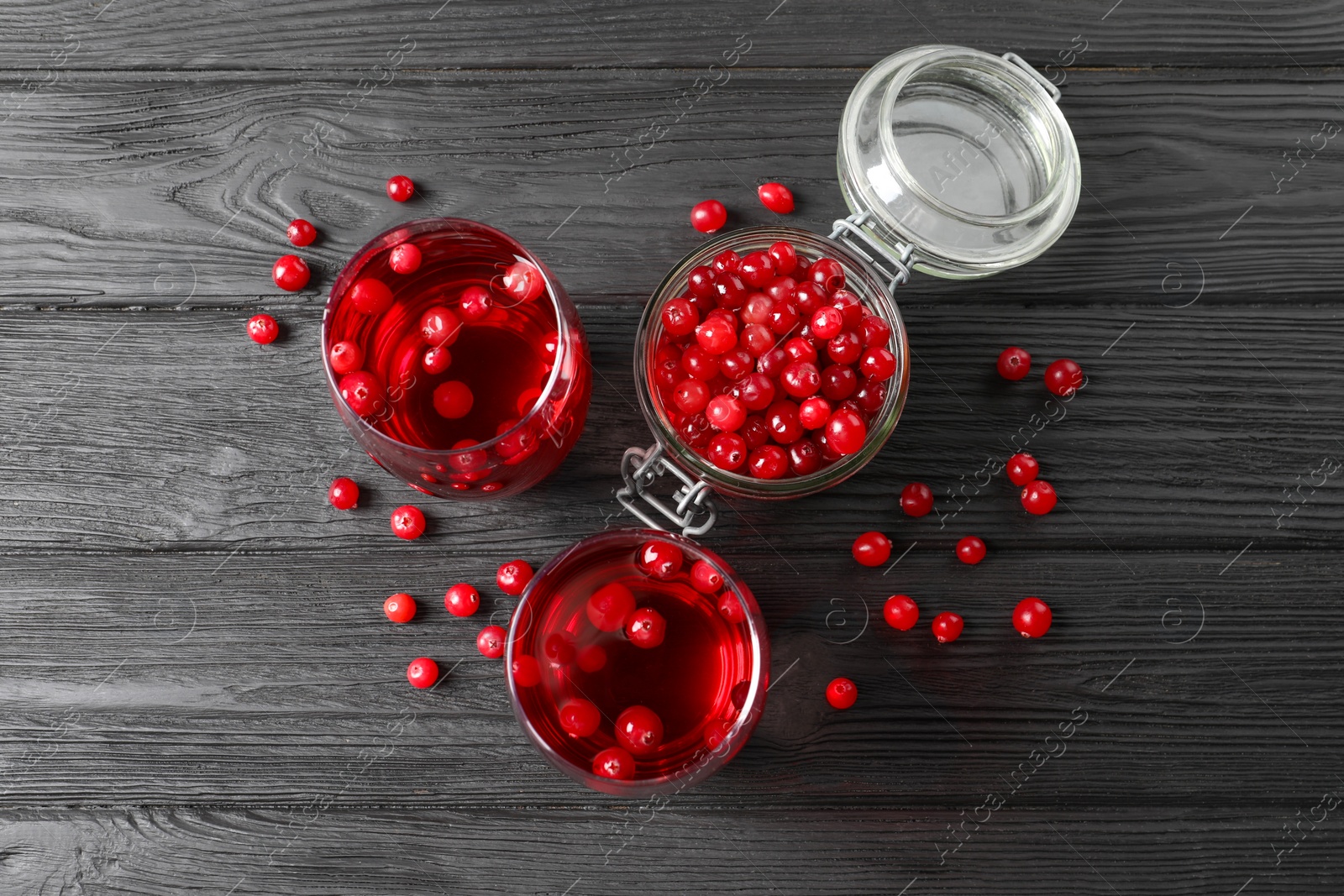 Photo of Tasty cranberry juice in glasses and fresh berries on black wooden table, flat lay