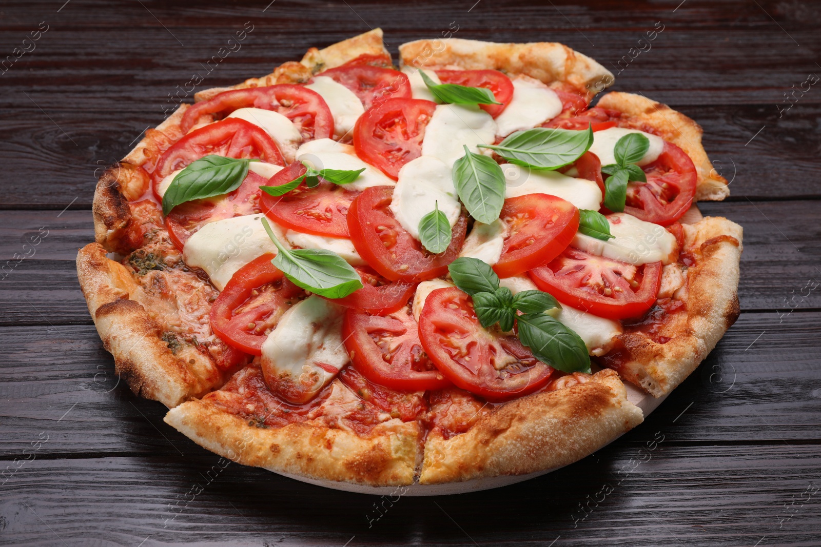 Photo of Delicious Caprese pizza with tomatoes, mozzarella and basil on dark wooden table, closeup