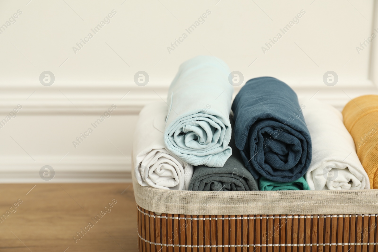 Photo of Basket with different rolled clothes on wooden table near white wall, space for text
