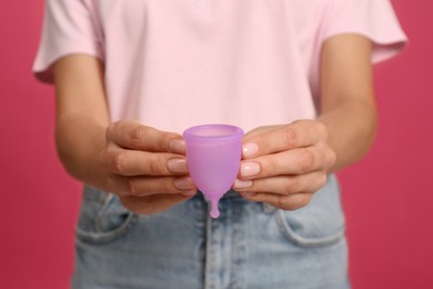 Young woman with menstrual cup on bright pink background, closeup