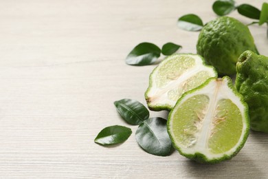 Whole and cut ripe bergamot fruits with green leaves on white wooden table, closeup. Space for text
