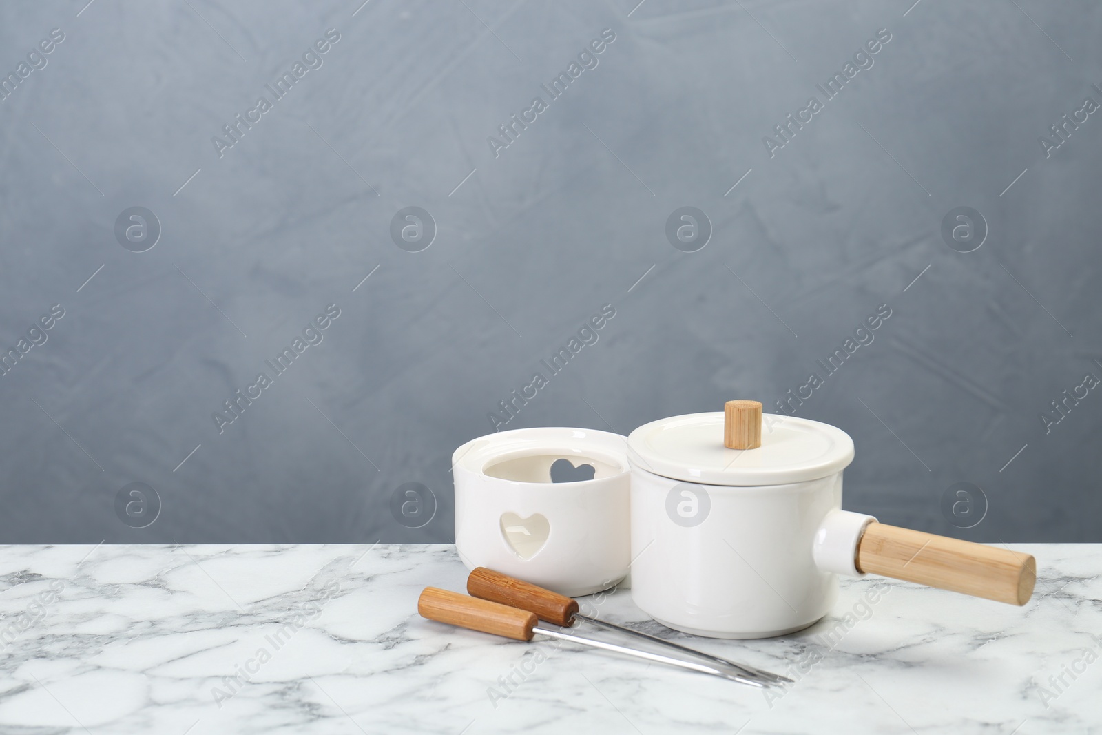 Photo of Fondue set on white marble table against light grey background, space for text