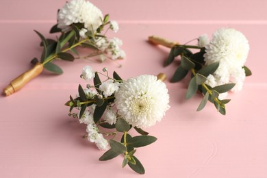Many small stylish boutonnieres on pink wooden table