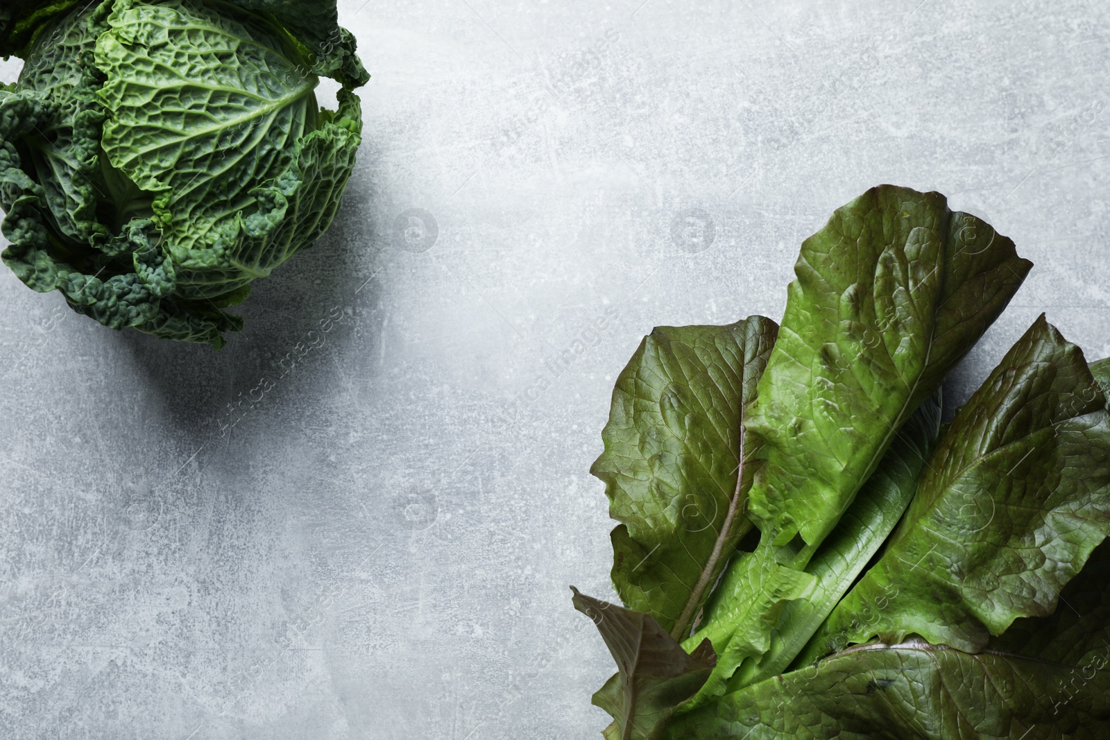 Photo of Fresh ripe savoy cabbage and cos lettuce on grey table, flat lay. Space for text